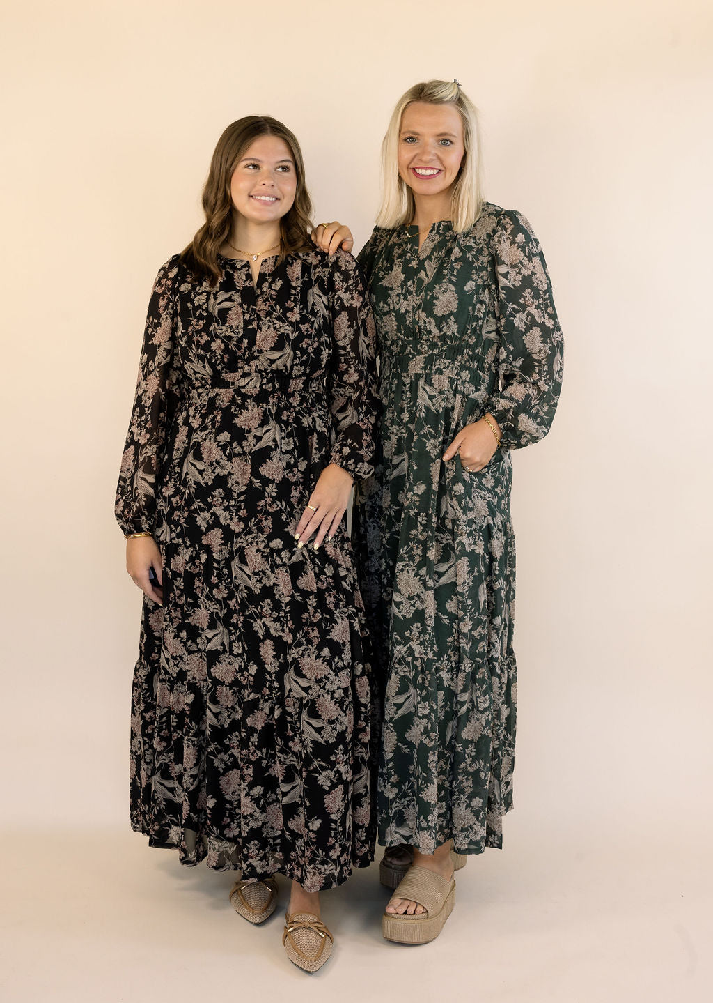 Two women modeling long-sleeve maxi dresses with a floral print, standing against a plain beige studio background.