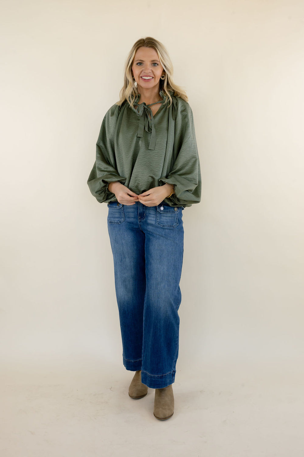 Full-length view of women's olive green long sleeve blouse with a tie neckline and voluminous sleeves, paired with wide leg denim jeans and neutral ankle boots.