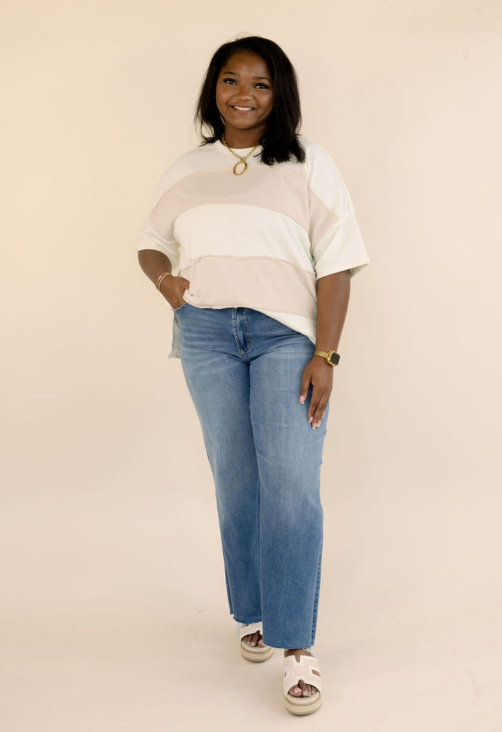 Full-length outfit featuring a plus size cream and taupe color block short sleeve top, wide leg blue jeans, and neutral sandals.