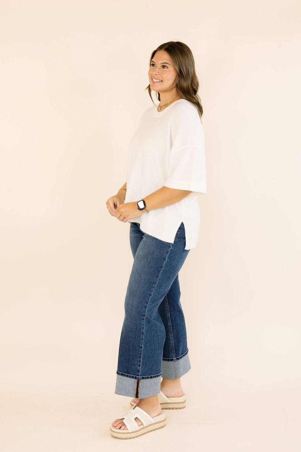 A woman modeling an off- white short-sleeve knit top and blue cuffed jeans against a plain beige studio background.