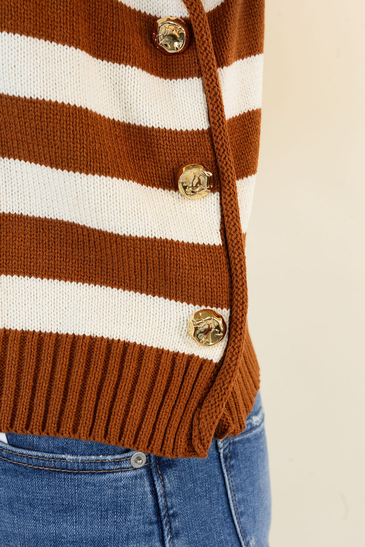 Close-up of a caramel and white striped knit cardigan with gold-tone buttons, worn over blue jeans against a plain light background.