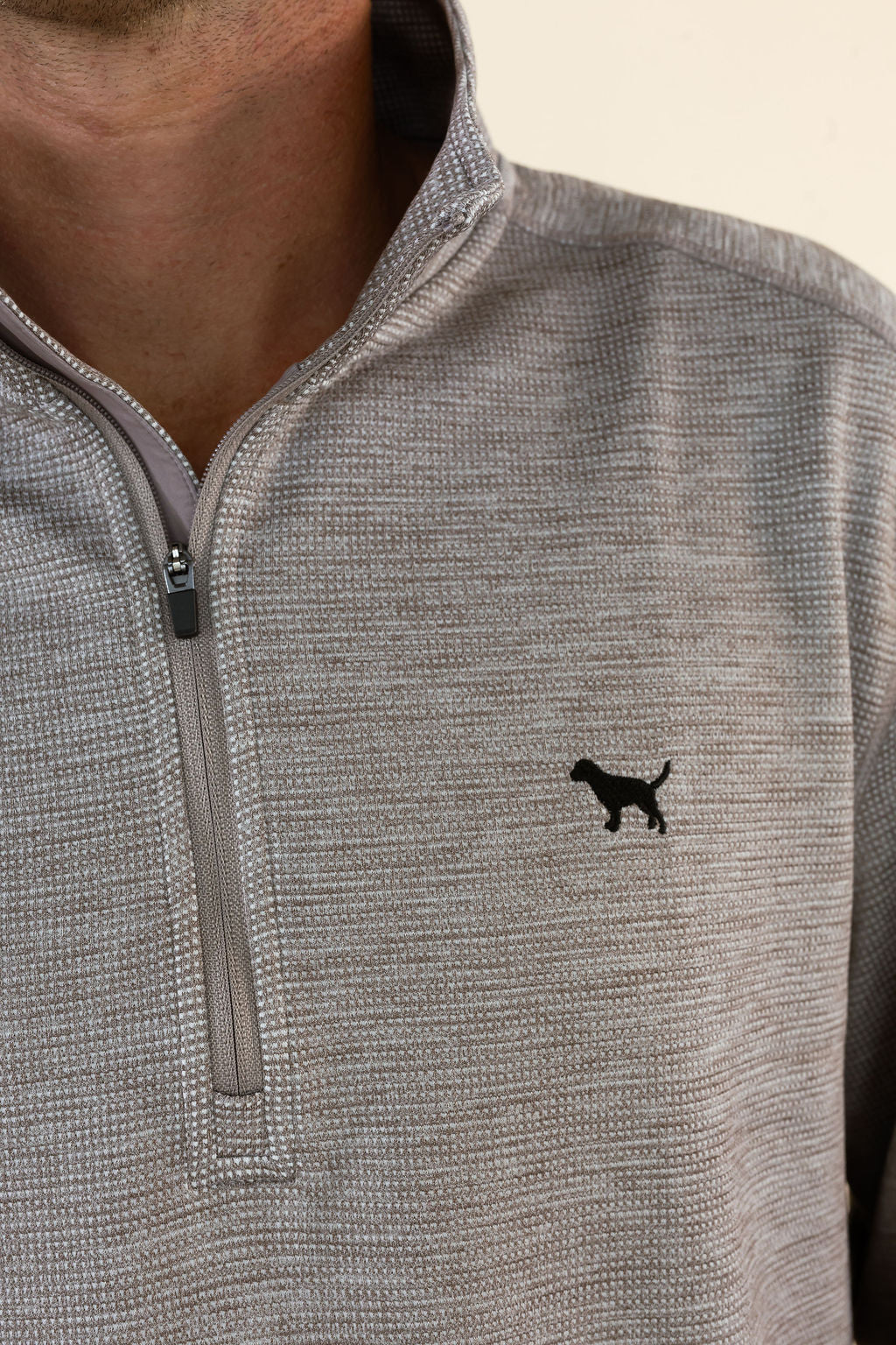 Close-up of a person wearing a heather brown quarter-zip pullover with a small black dog silhouette logo on the left chest.