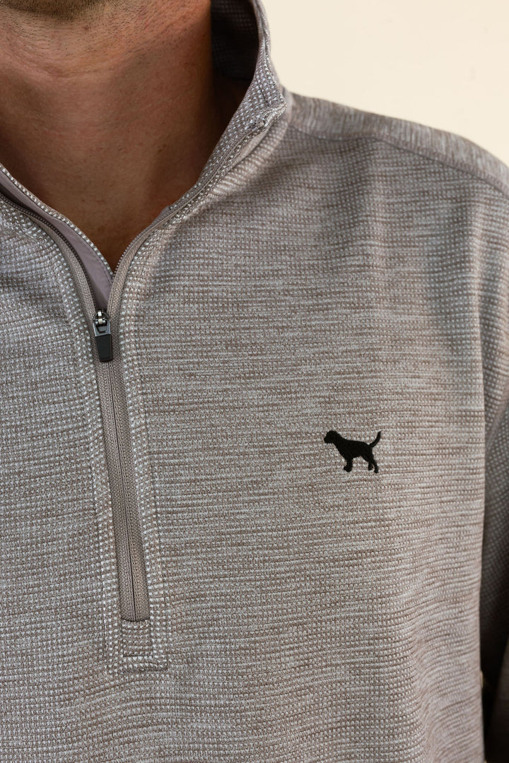 Close-up of a person wearing a heather brown quarter-zip pullover with a small black dog silhouette logo on the left chest.