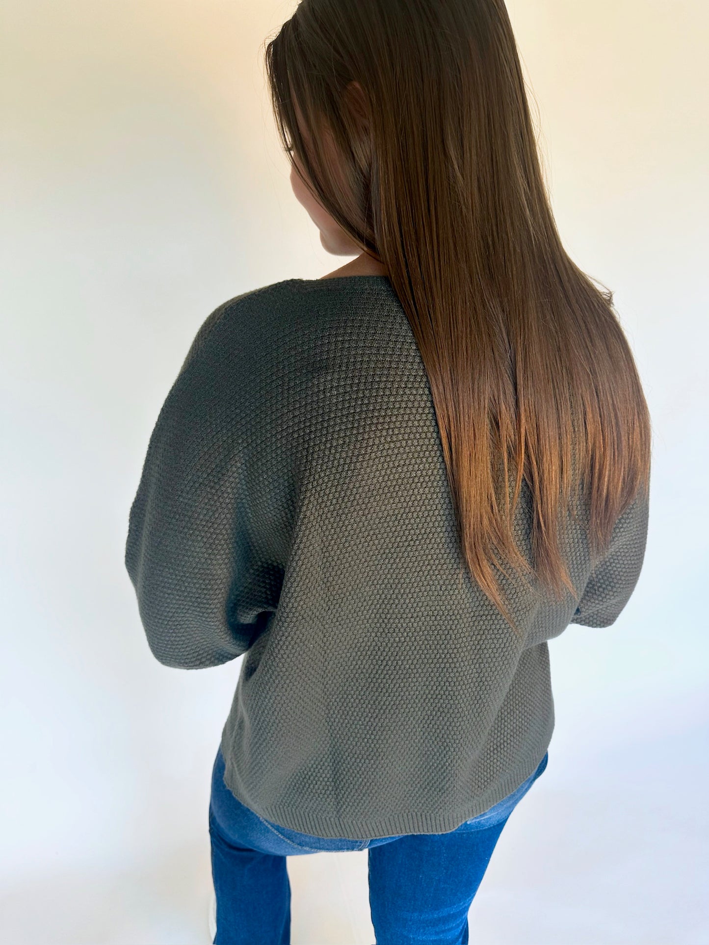 Person wearing a green sweater and blue jeans against a white background