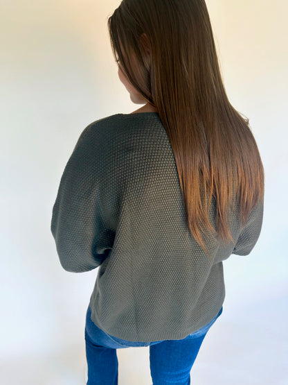 Person wearing a green sweater and blue jeans against a white background