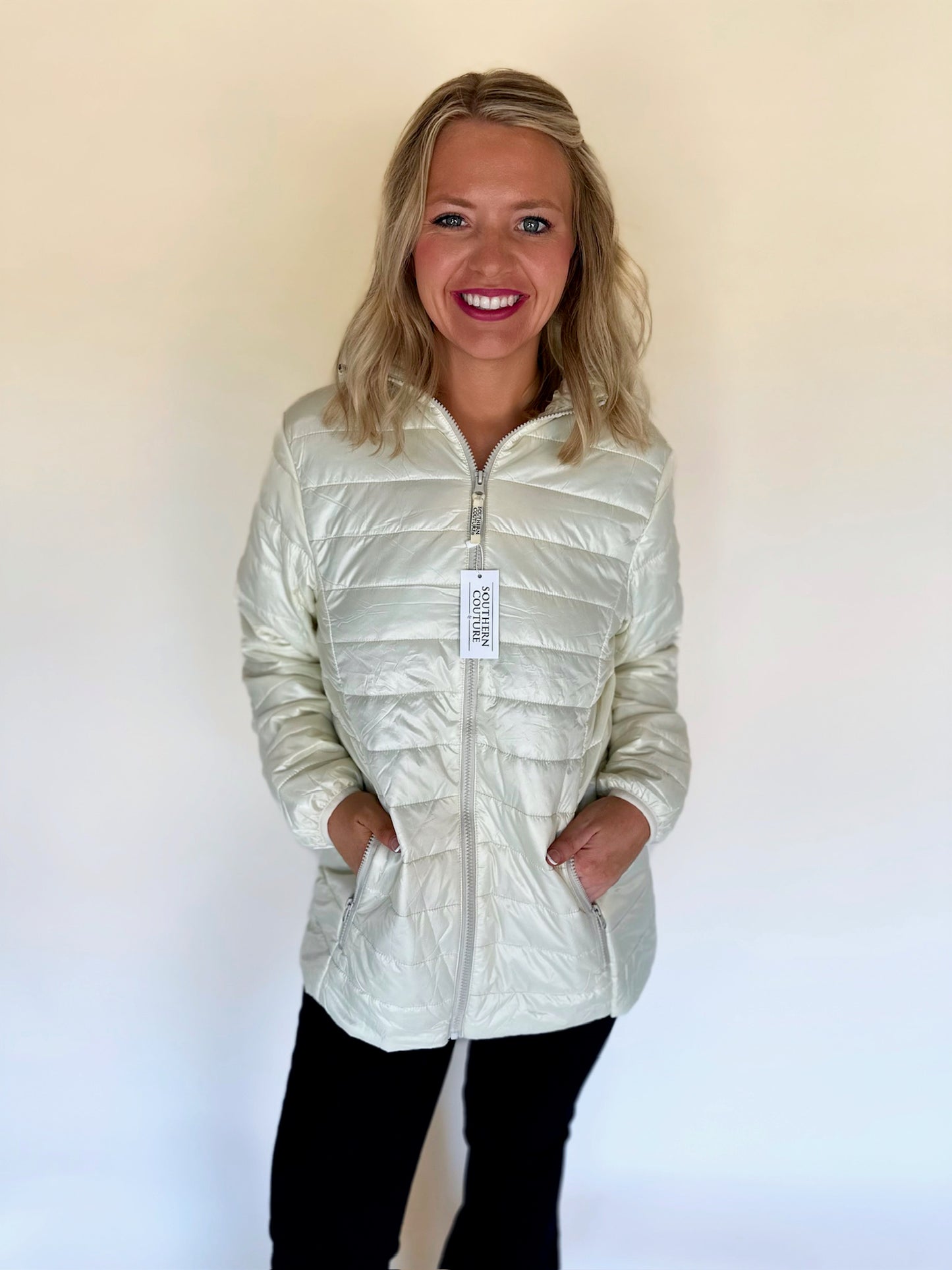 Woman wearing a light-colored puffer jacket with a visible brand tag on a plain background