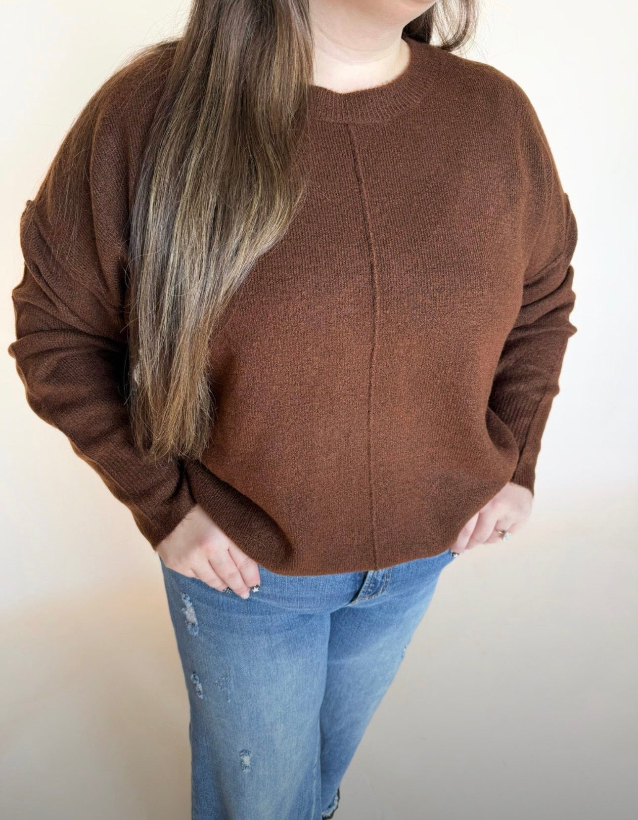 Person wearing a brown sweater and blue jeans against a plain background