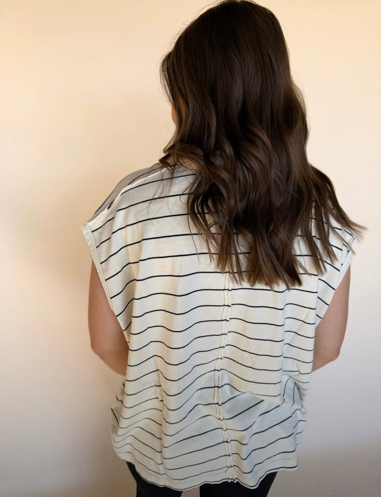 “Back view of a cream and black striped top featuring a gathered seam detail down the center.