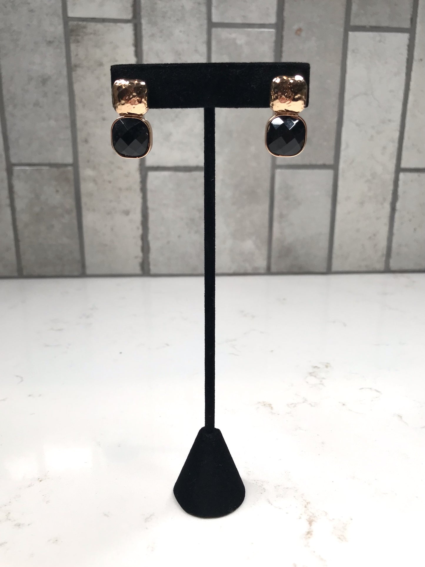 Gold hammered stud earrings with faceted black drop stones shown on a tall black jewelry stand.