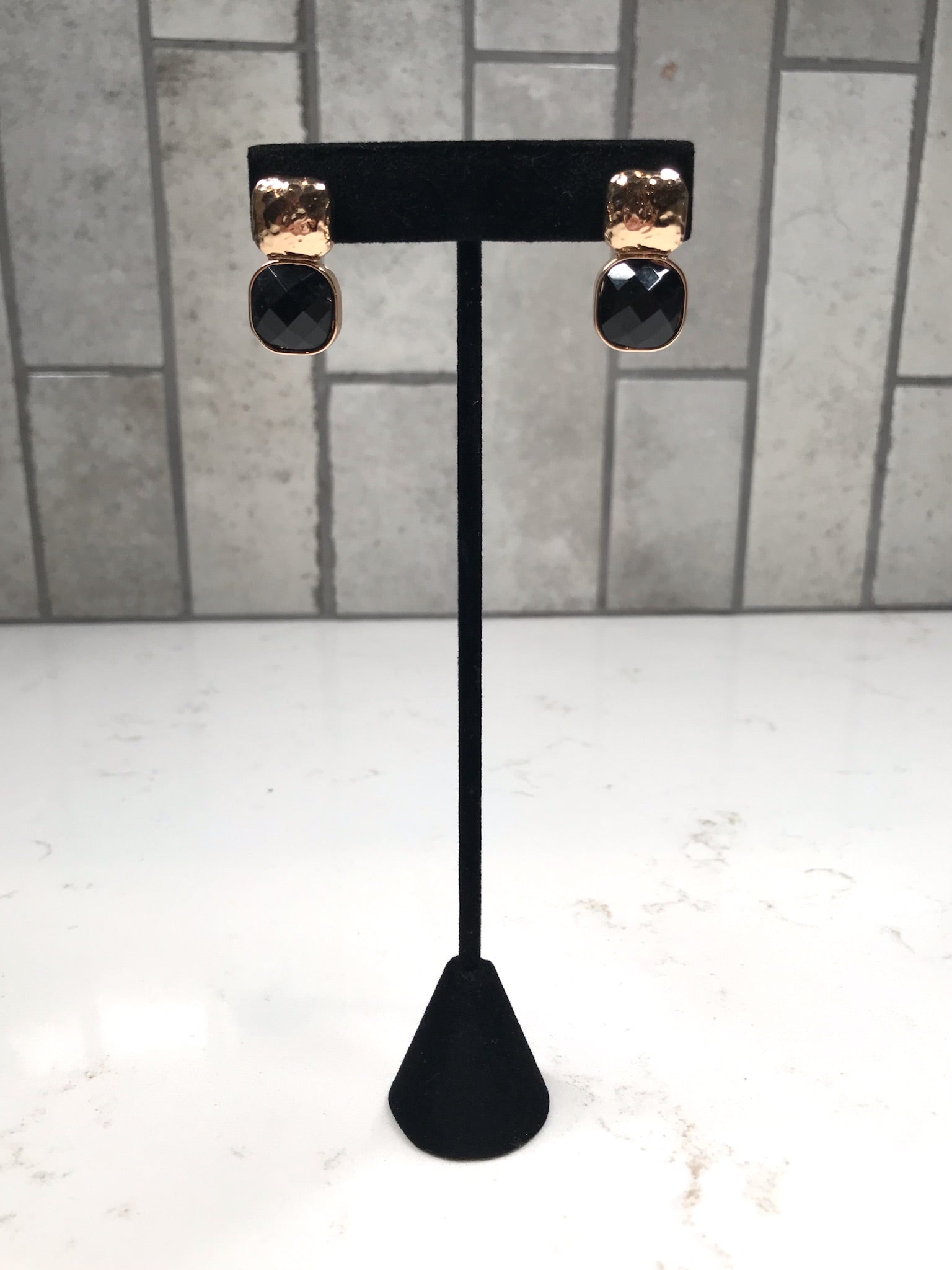 Gold hammered stud earrings with faceted black drop stones shown on a tall black jewelry stand.