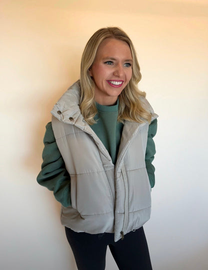 Woman wearing a light gray vest over a green sweater against a plain background
