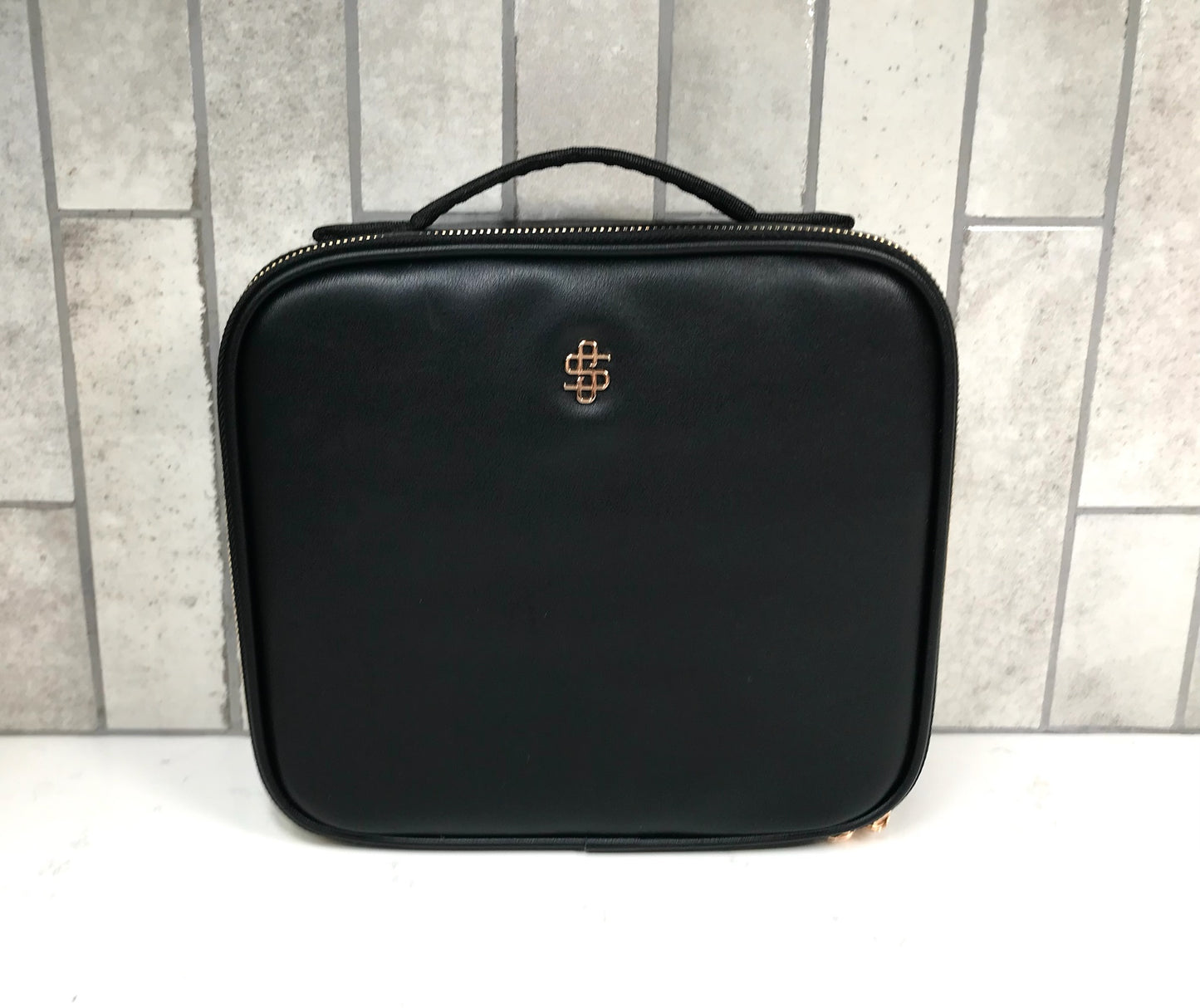Black travel cosmetic case with a logo on a tiled wall background