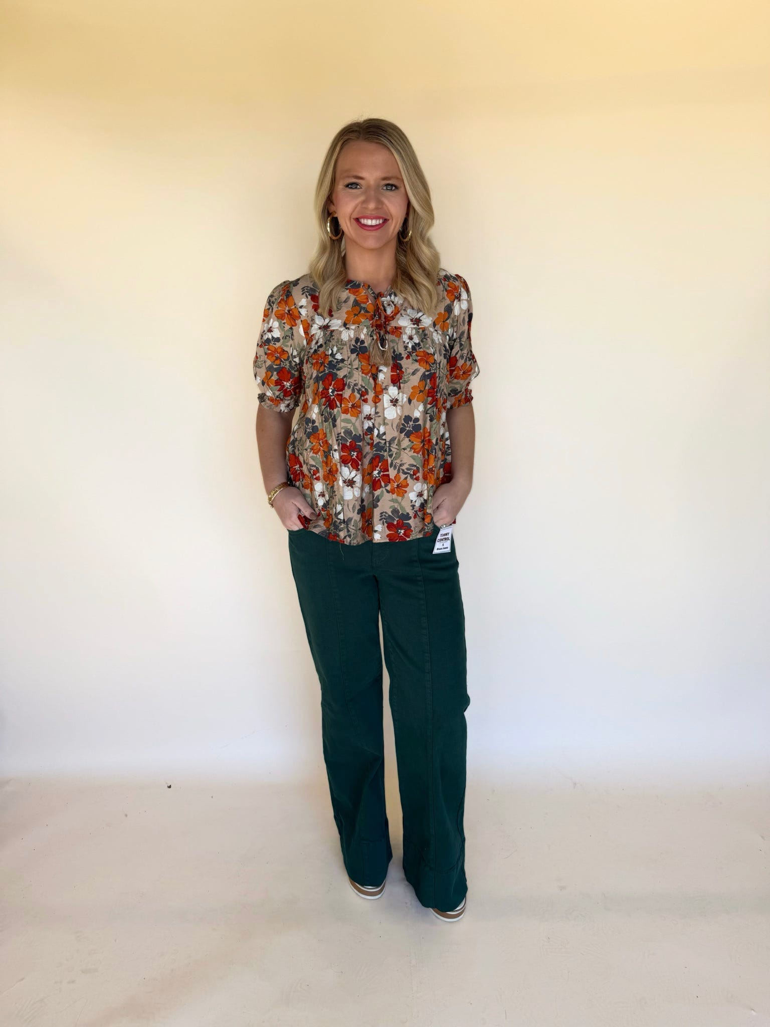 Woman wearing a fall floral blouse with puff sleeves paired with dark green wide-leg pants, standing against a neutral background.