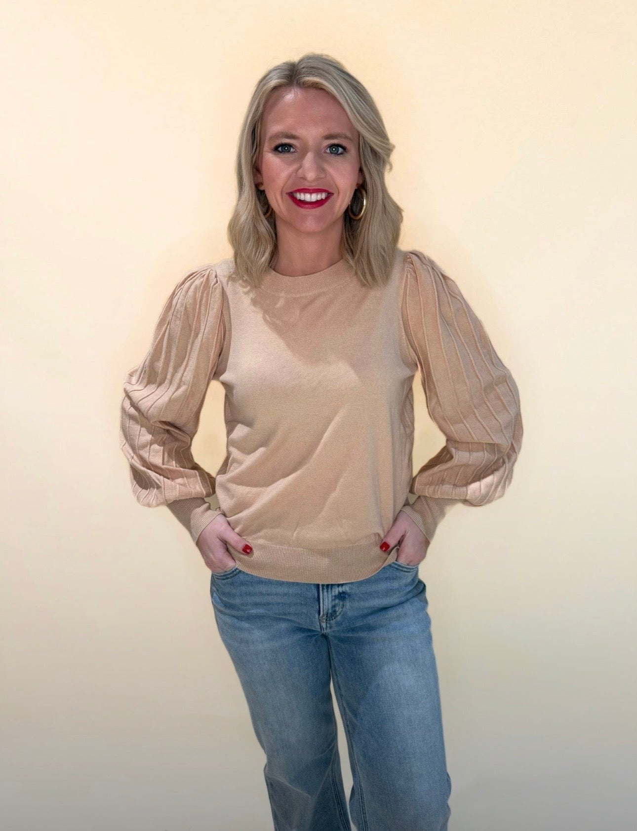 Woman wearing beige puff sleeve knit sweater with textured sleeves, paired with light wash denim jeans.