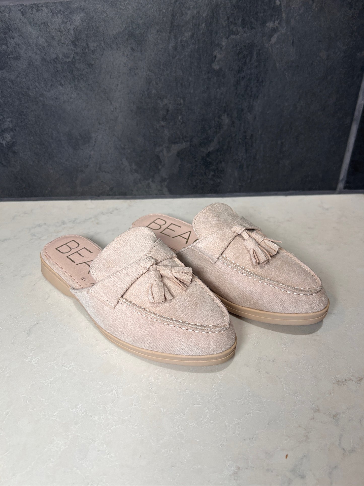 Pair of beige loafers with tassels on a gray surface with a dark gray background