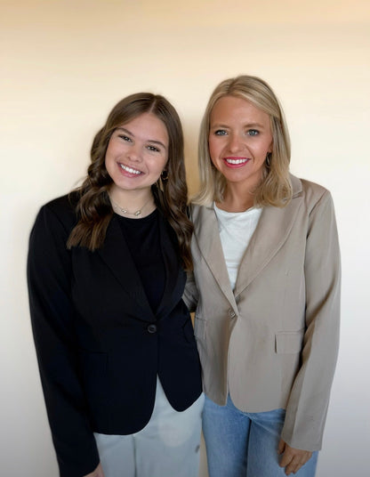 Two women standing side by side in a blazer against a plain background