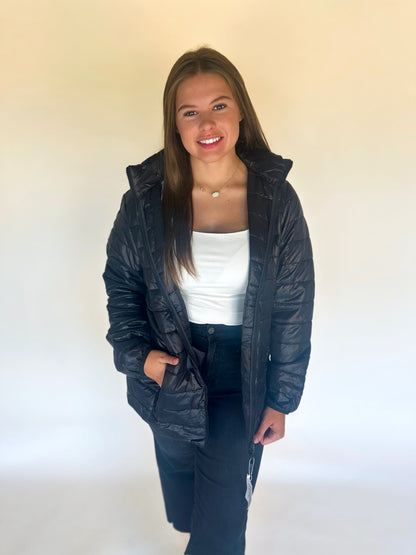 Person wearing a black puffer jacket over a white shirt on a plain background