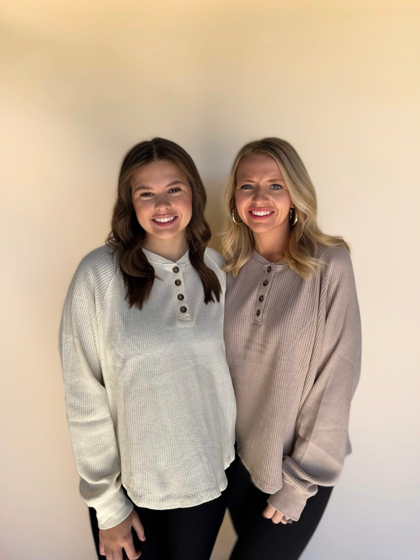 Two women wearing light-colored sweaters standing against a plain background