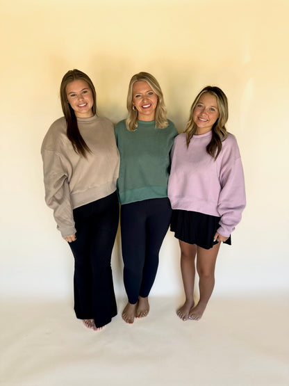 Three women standing together wearing casual outfits against a plain background