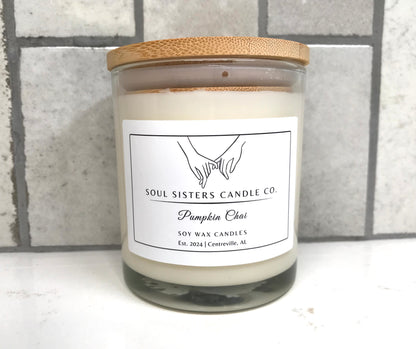 Scented candle in a glass jar with a wooden lid on a white surface with a gray tiled background