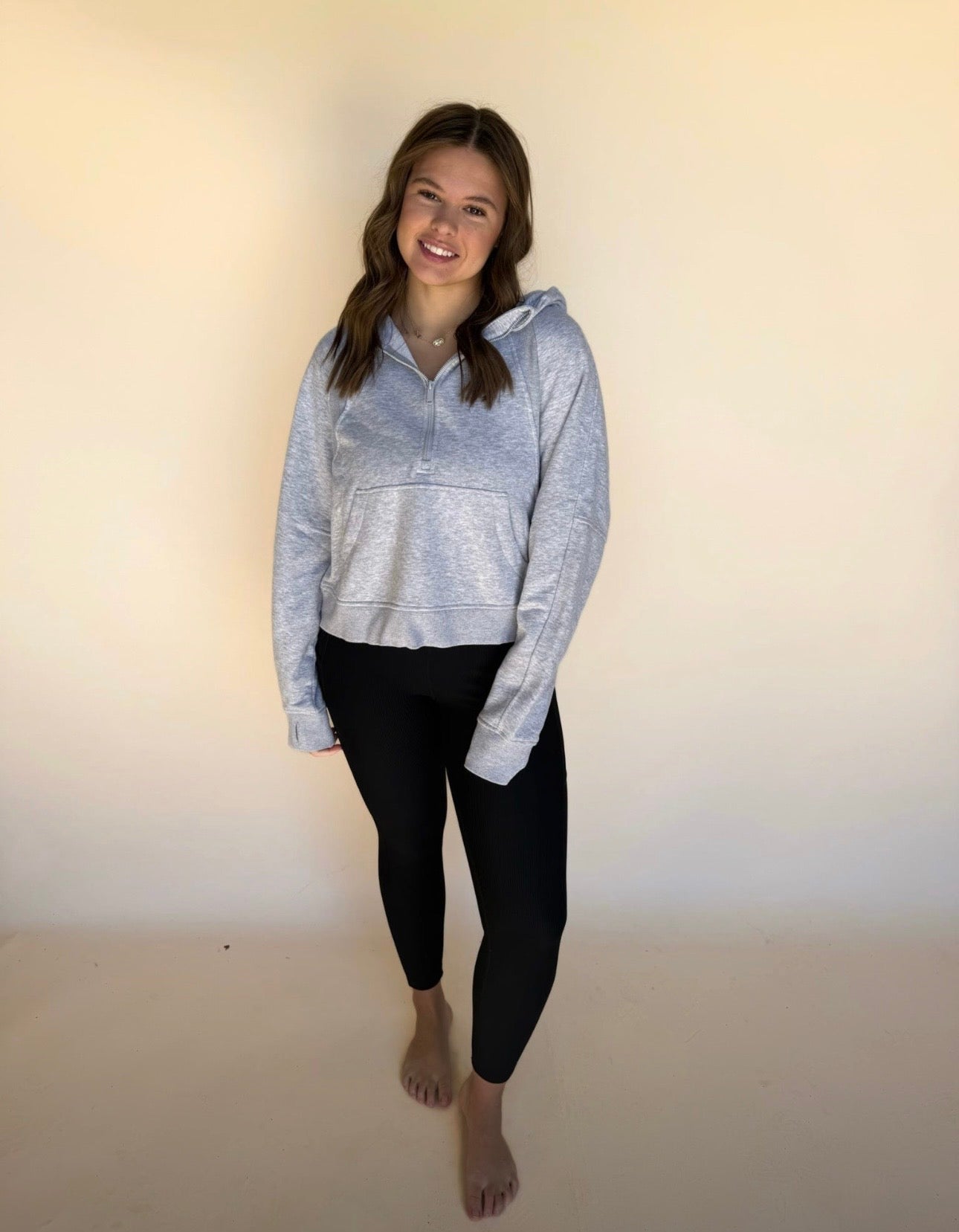 Woman wearing a gray hoodie and black leggings against a plain background
