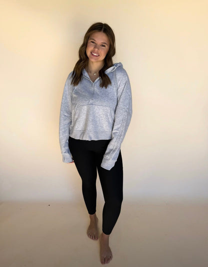 Woman wearing a gray hoodie and black leggings against a plain background