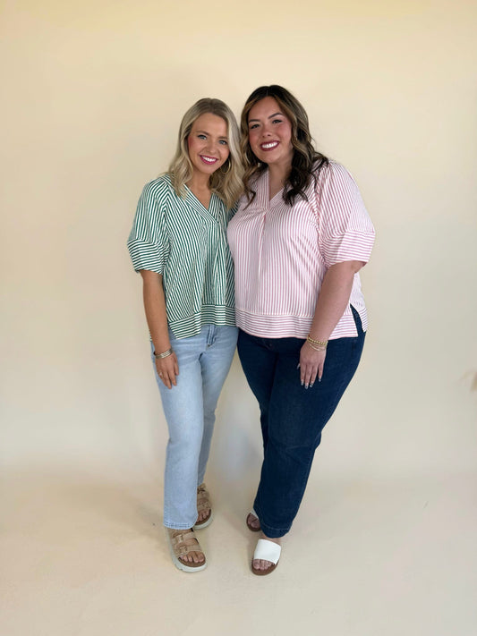 Two women modeling the Zinnia striped V-neckline top in green and pink, featuring a relaxed fit and lightweight woven fabric, styled with denim jeans against a neutral backdrop.