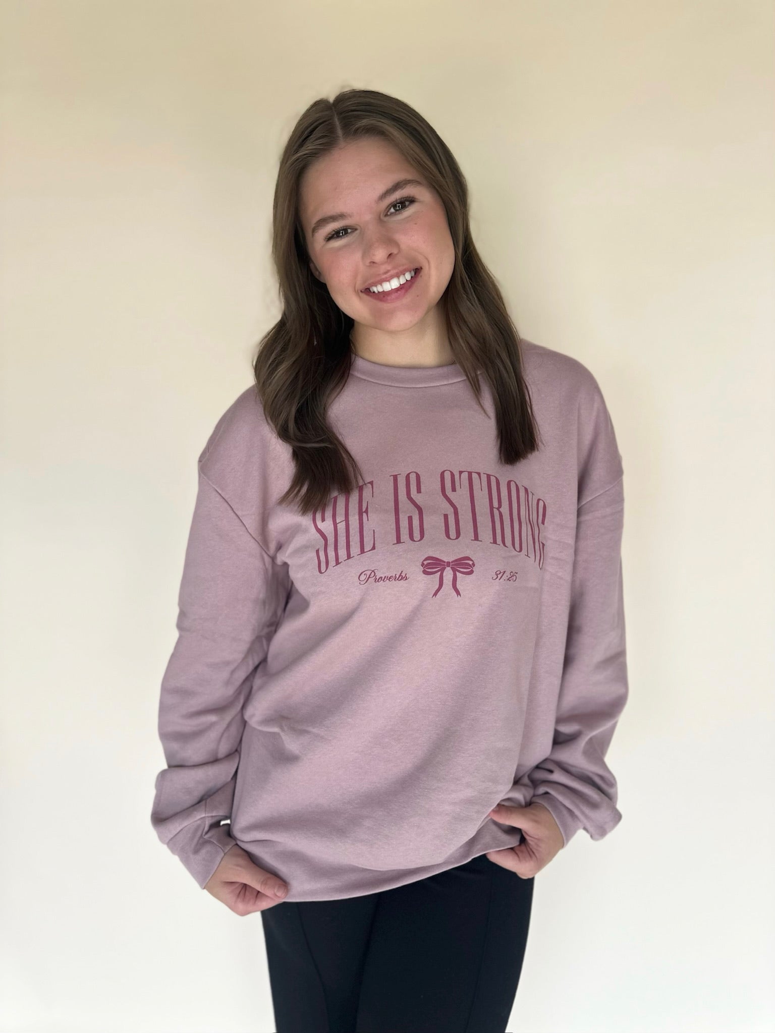 Person wearing a pink sweatshirt with 'She is Strong' text on a plain background