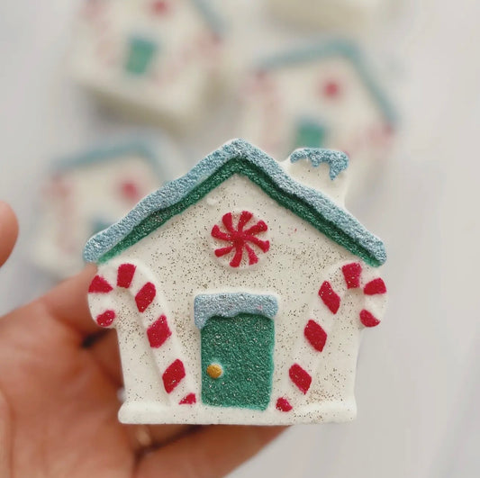 Festive cottage bath bomb designed like a Christmas gingerbread house with red candy canes, peppermint swirl, green door and shimmer accents — perfect for winter gifts and stocking stuffers