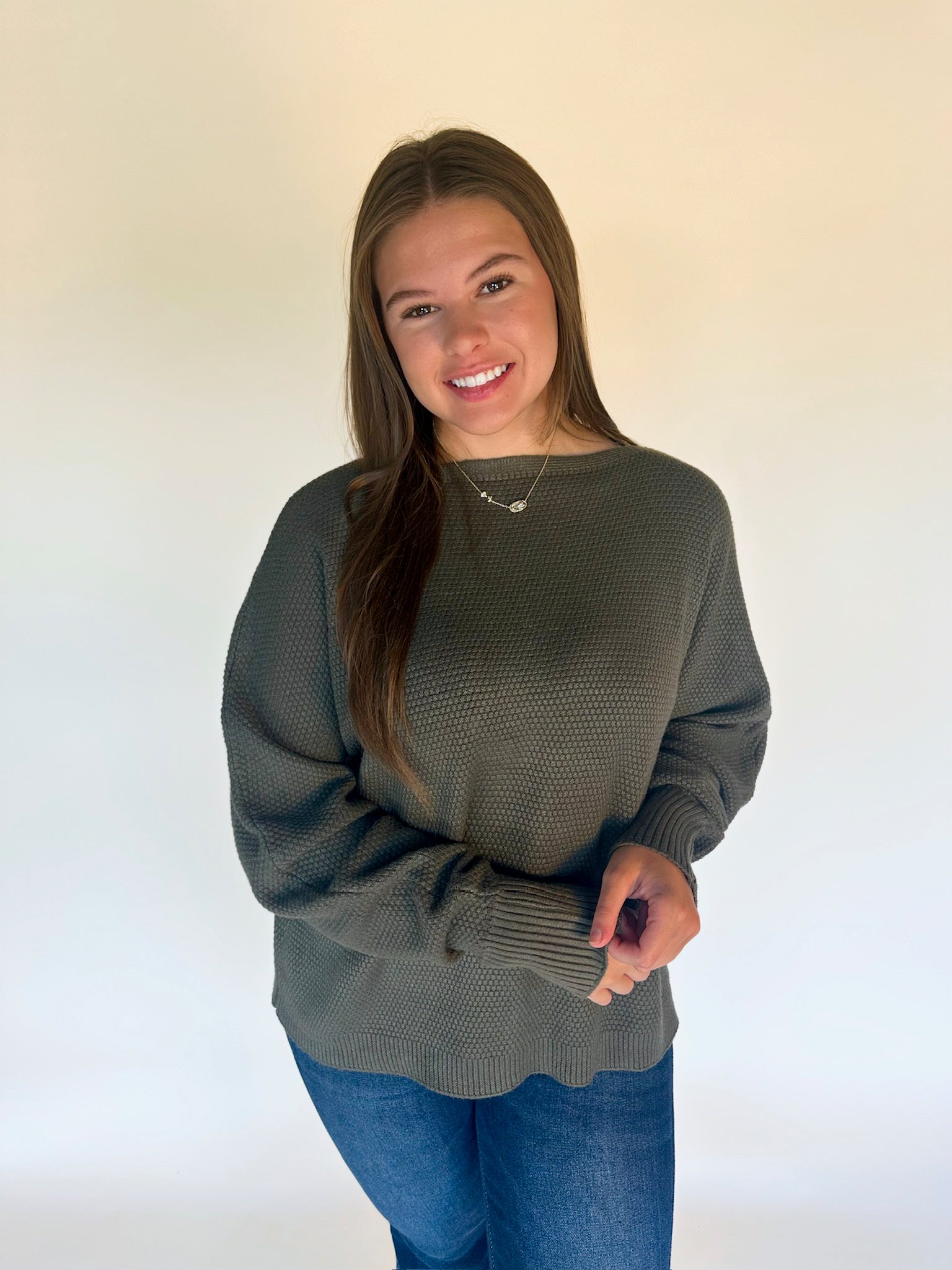 Woman wearing a green sweater and blue jeans against a white background