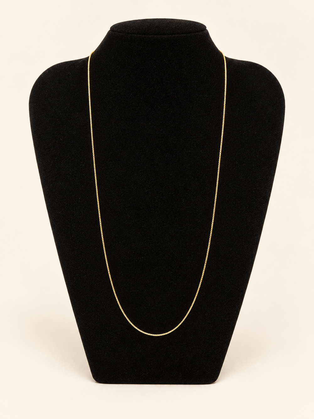 Delicate long gold chain necklace displayed on a black velvet jewelry bust against a cream studio background.