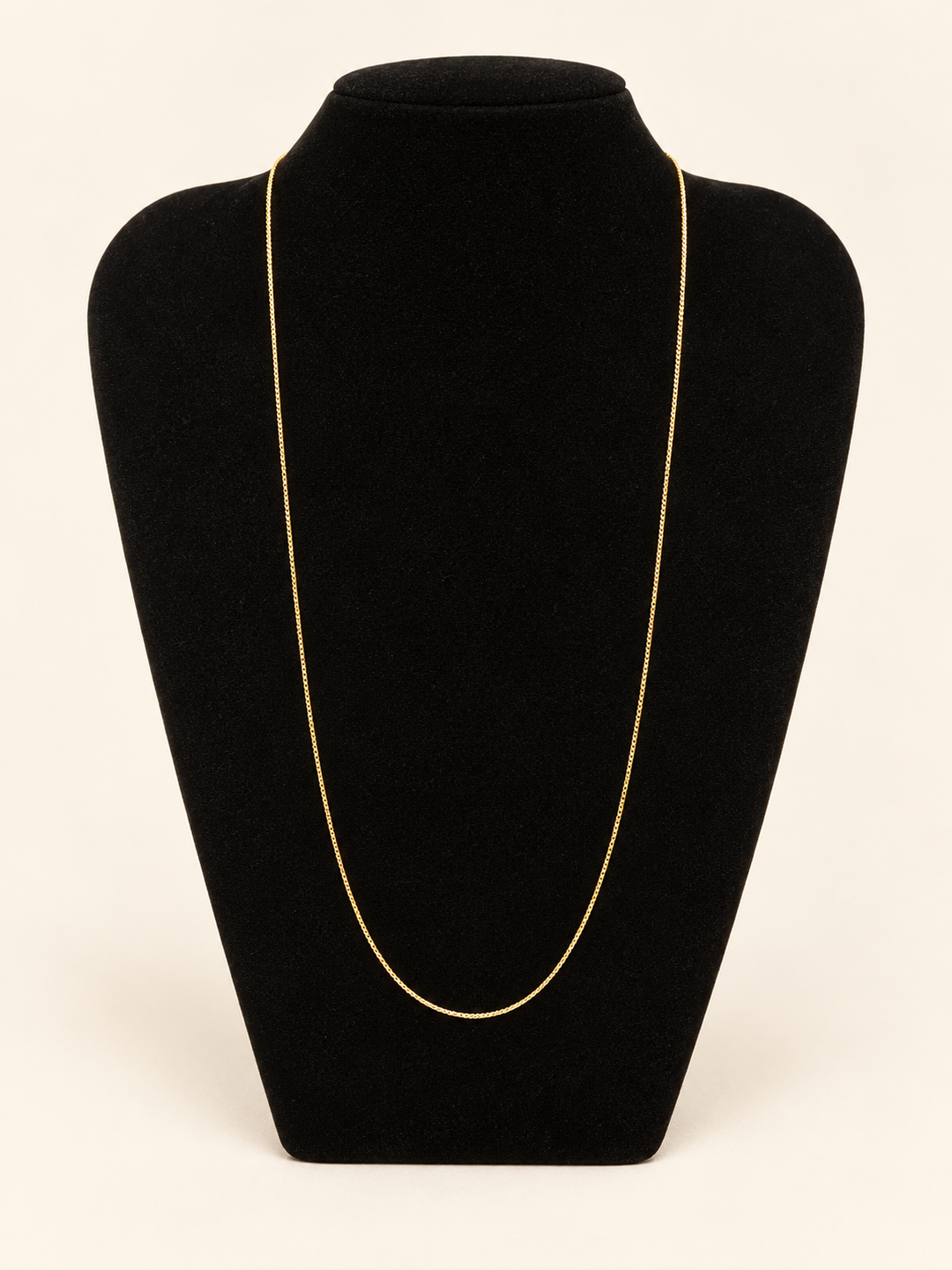 Delicate long gold chain necklace displayed on a black velvet jewelry bust against a cream studio background.