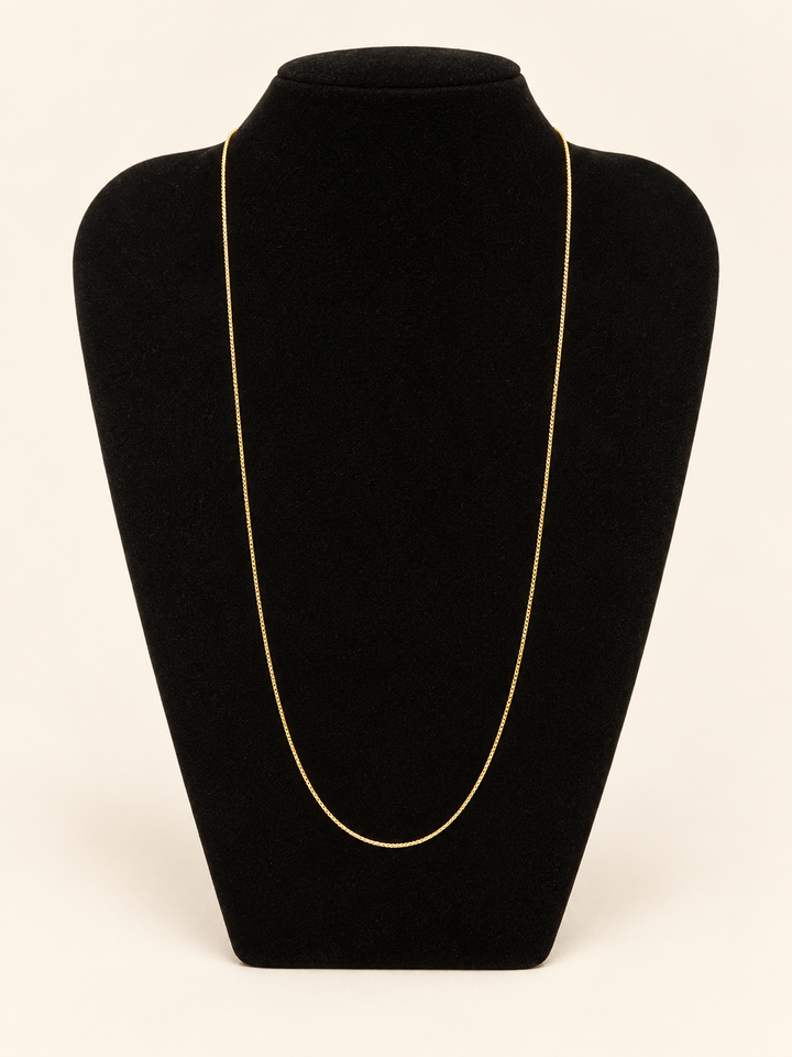 Delicate long gold chain necklace displayed on a black velvet jewelry bust against a cream studio background.