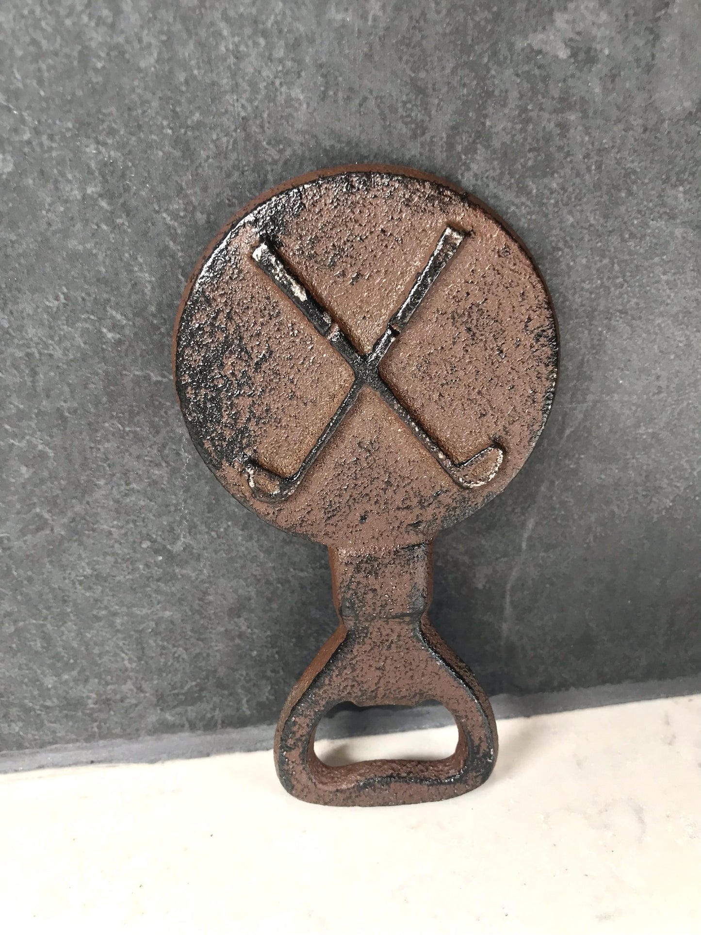Black metal bottle opener with crossed golf clubs on a wooden background