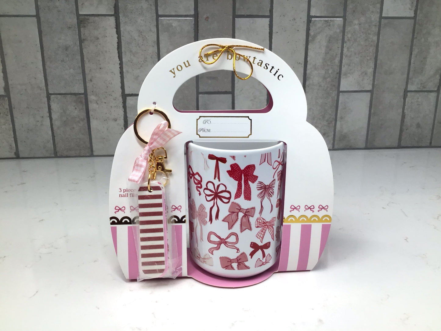 Pink bow-pattern ceramic mug packaged in holiday gift box with striped nail file keychain and pink ribbon.