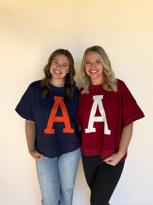 Two women wearing oversized shirts with large letters 'A' on a plain background
