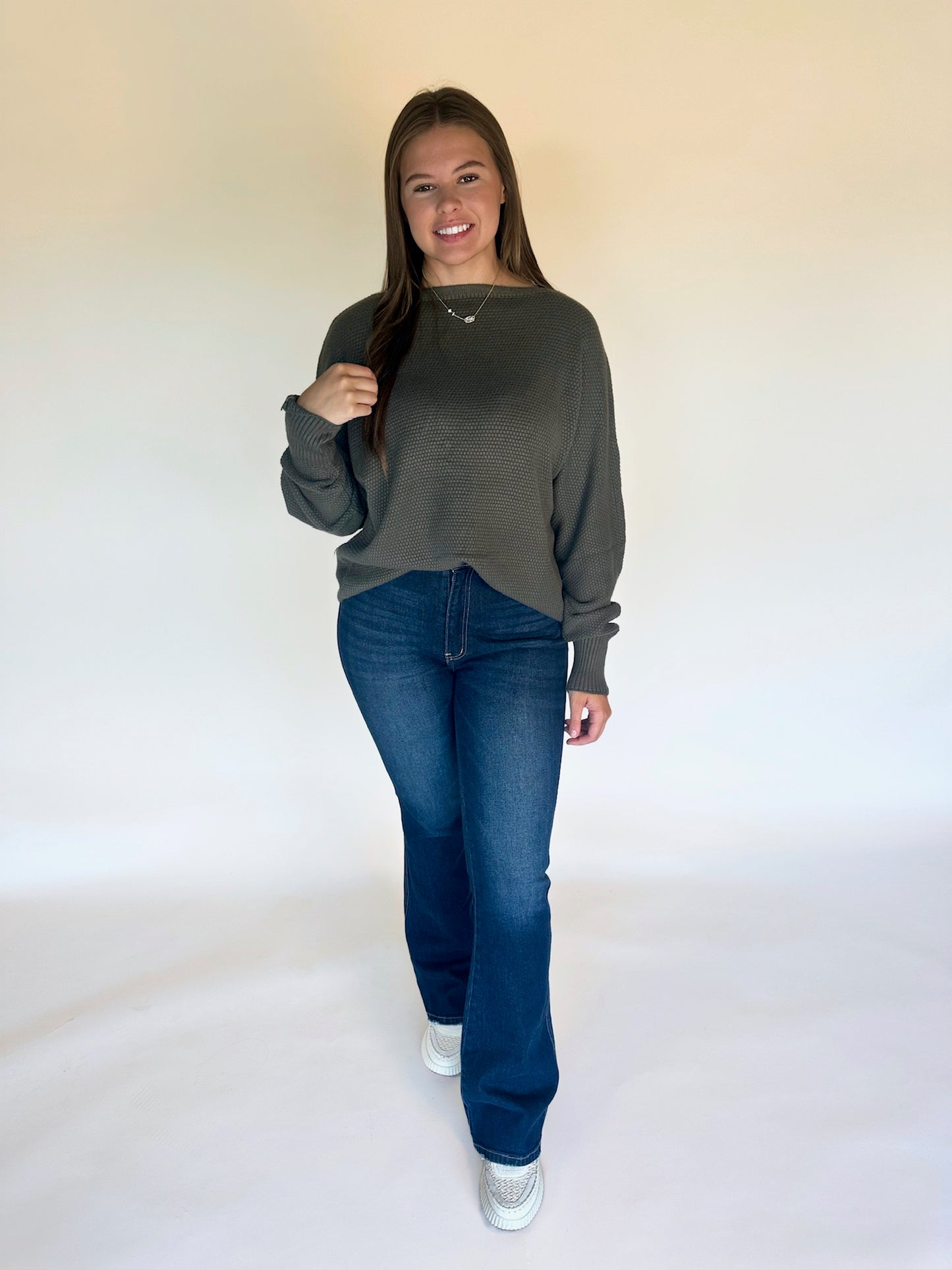Woman wearing a green sweater and blue jeans against a white background