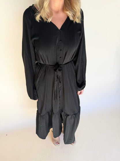 Person wearing a black dress with long sleeves and a belt on a white background