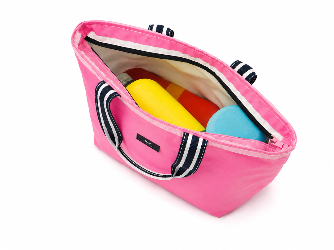 A pink tote bag with black and white striped handles, shown open with colorful cylindrical items inside, photographed on a clean white background.