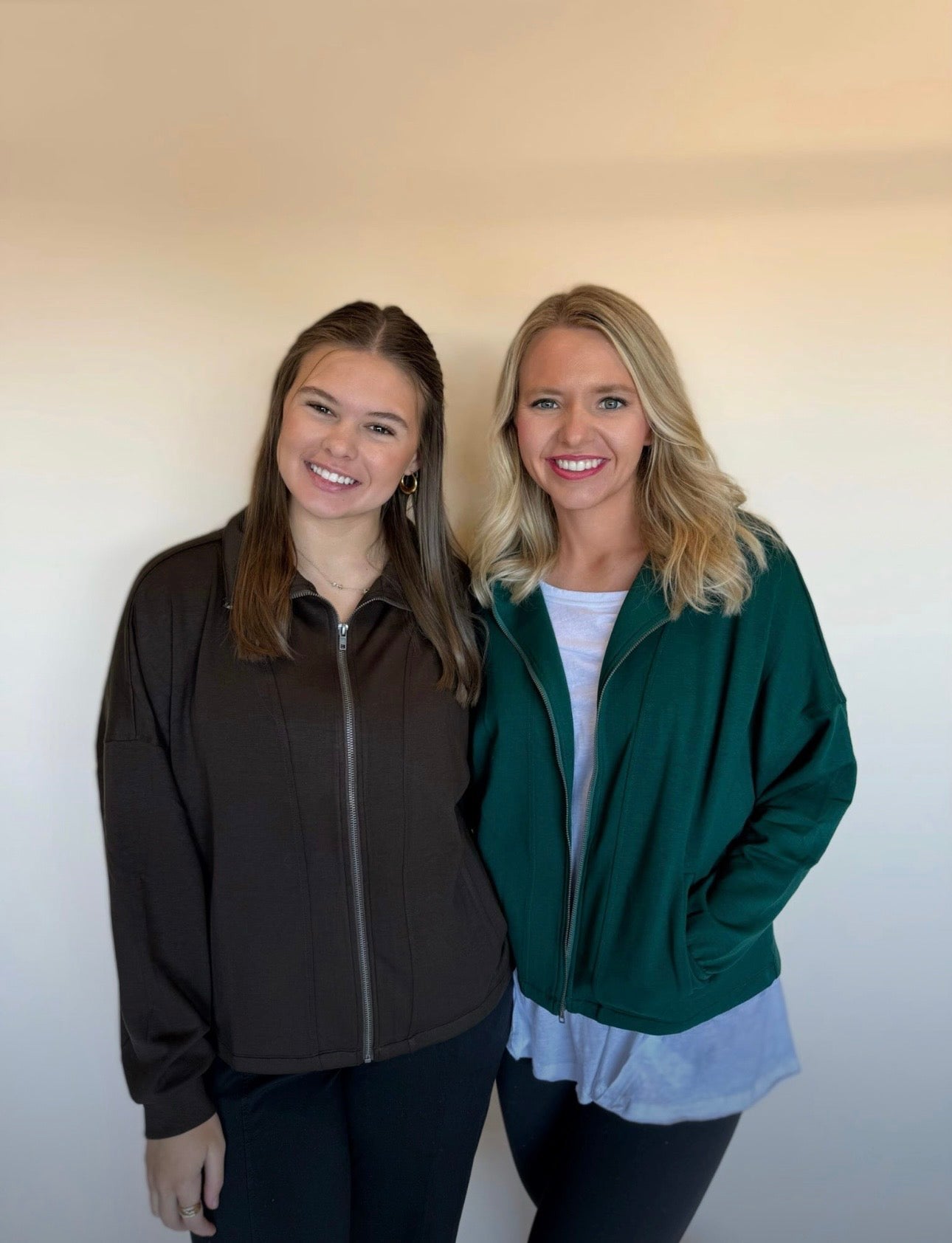 Two women standing side by side wearing zip-up jackets against a plain background