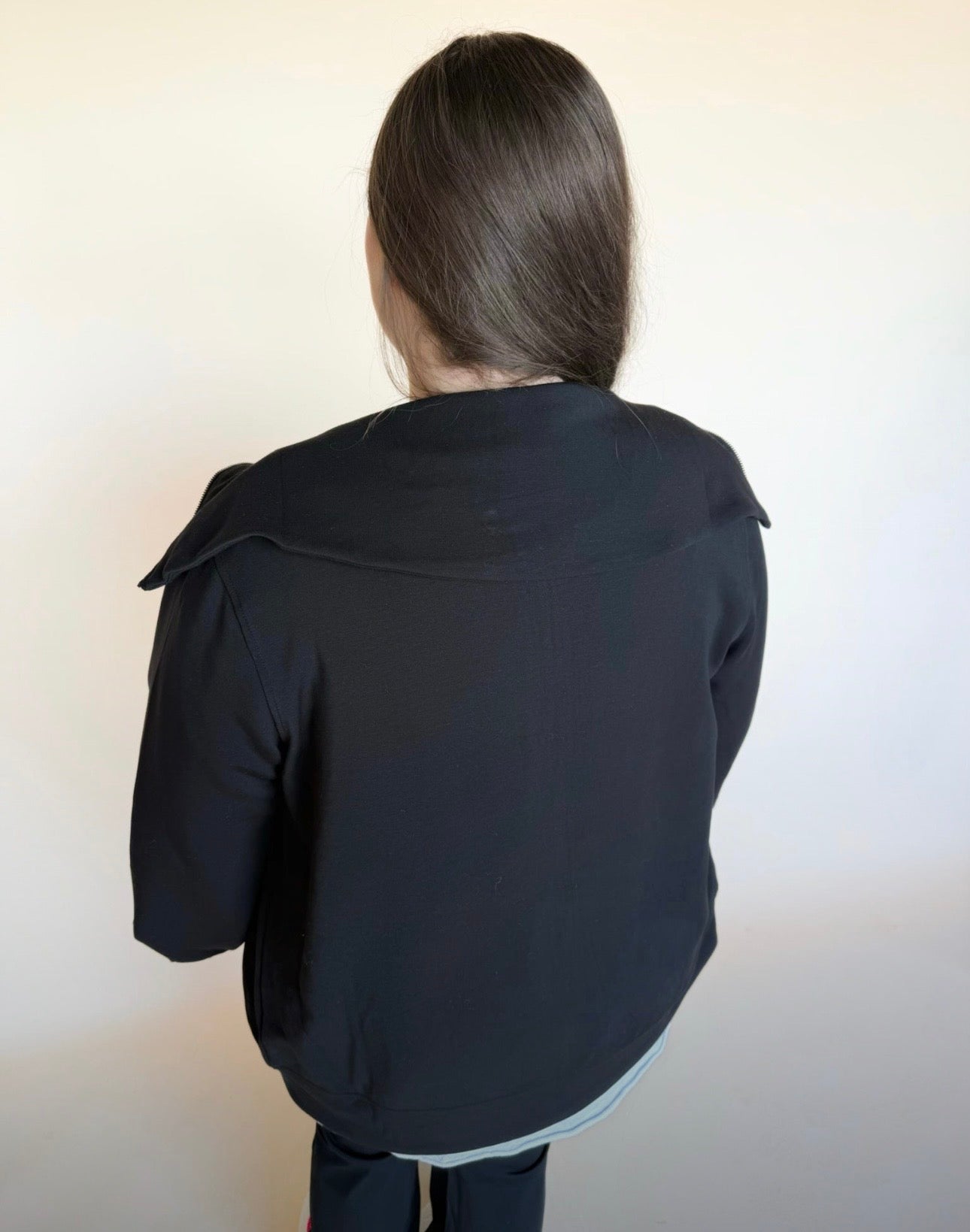 Person wearing a black jacket with a bow detail on the back against a plain background