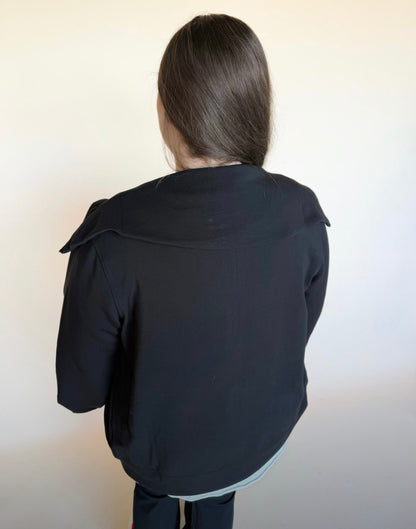 Person wearing a black jacket with a bow detail on the back against a plain background