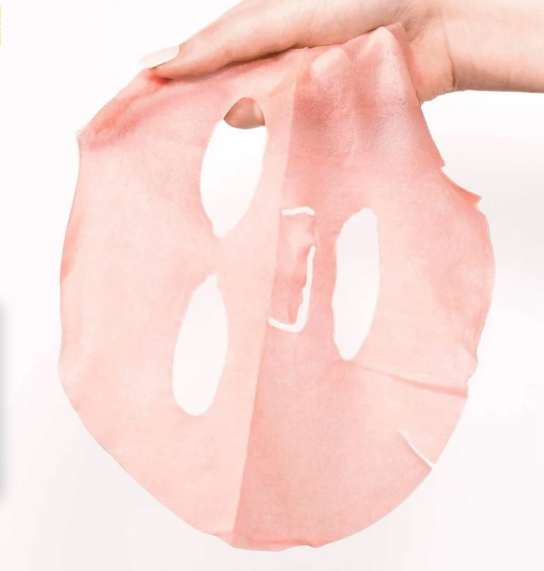 Pink face mask sheet held by a hand on a white background