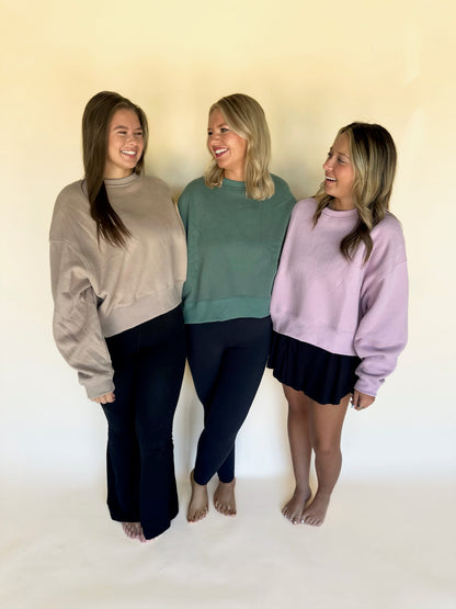Three women wearing different colored sweaters against a plain background