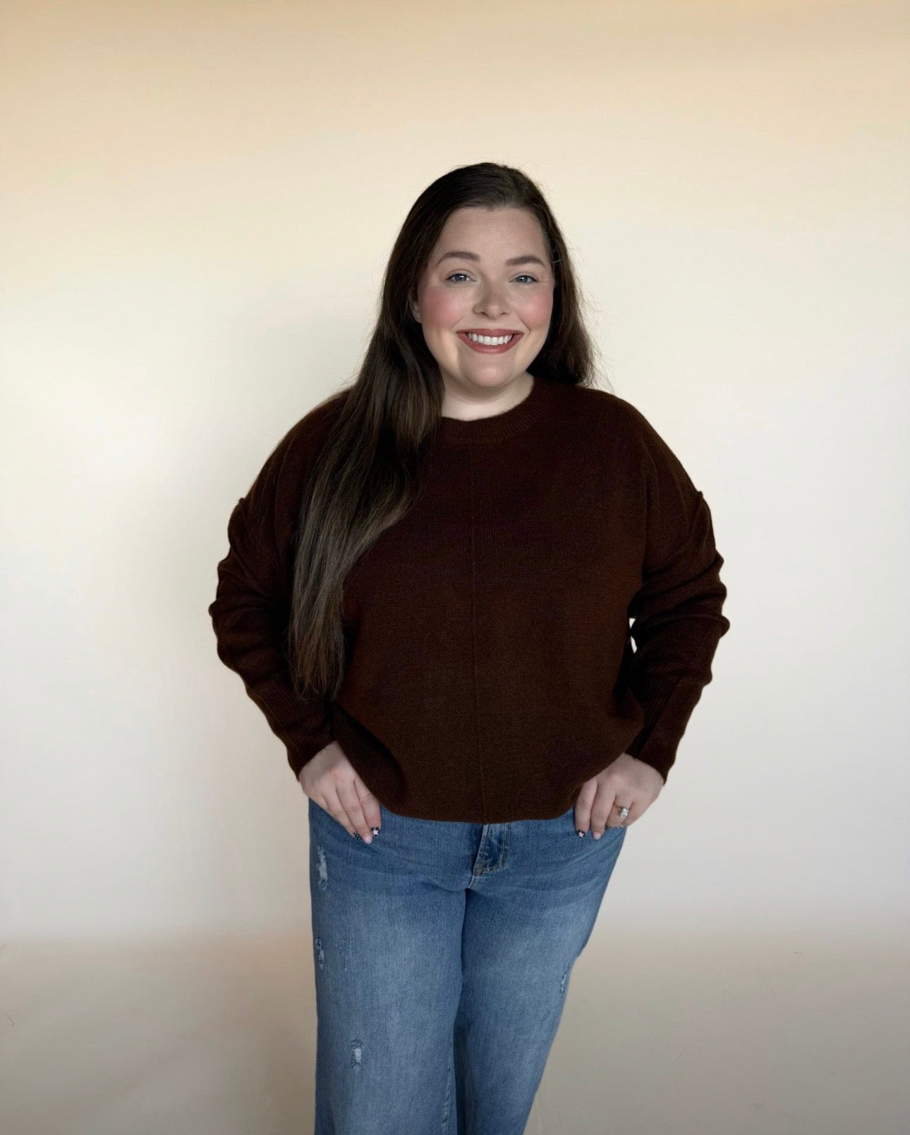 Person wearing a brown sweater and blue jeans against a plain background