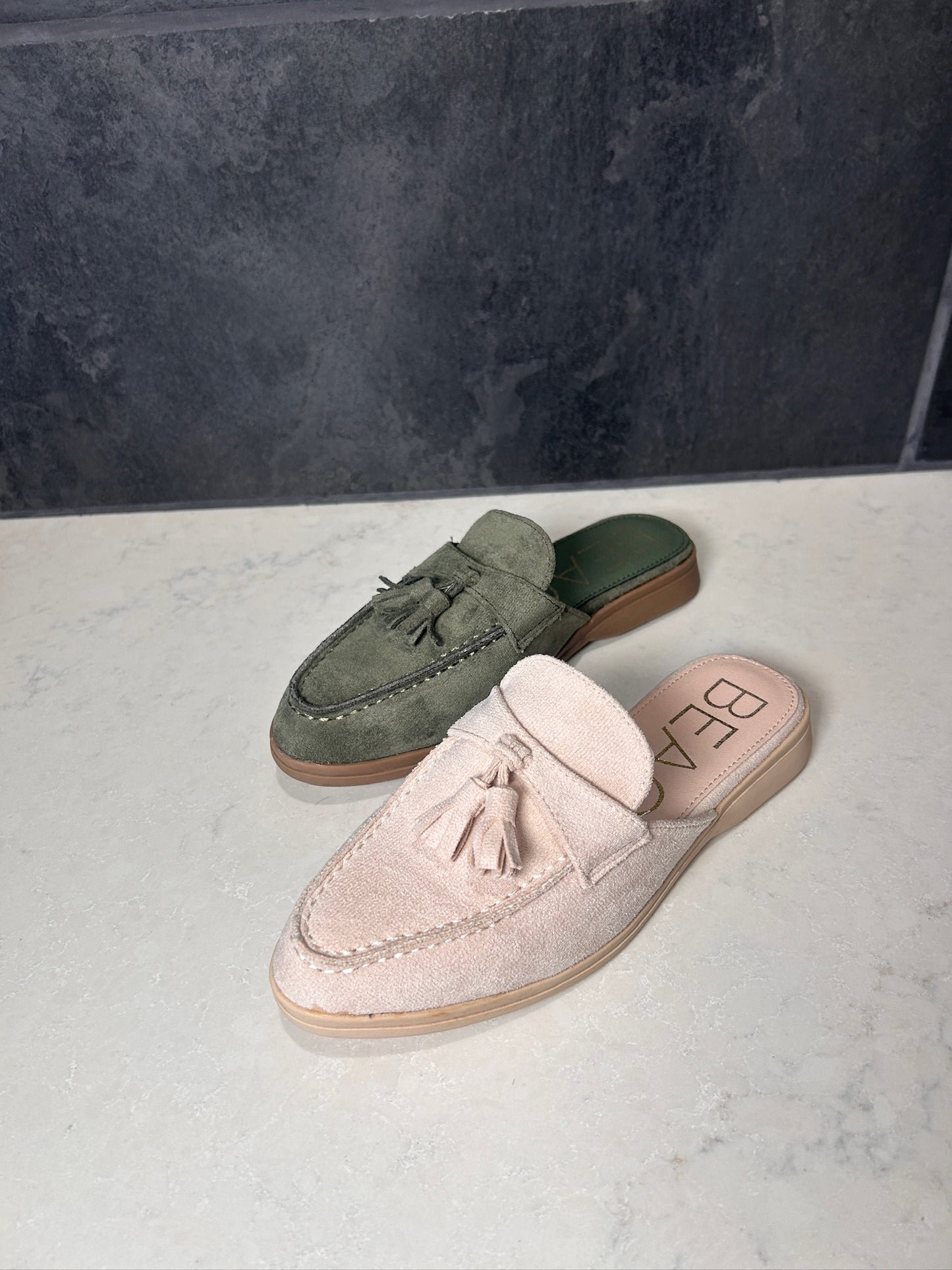Pair of green loafers and pink mules on a marble surface with a dark background