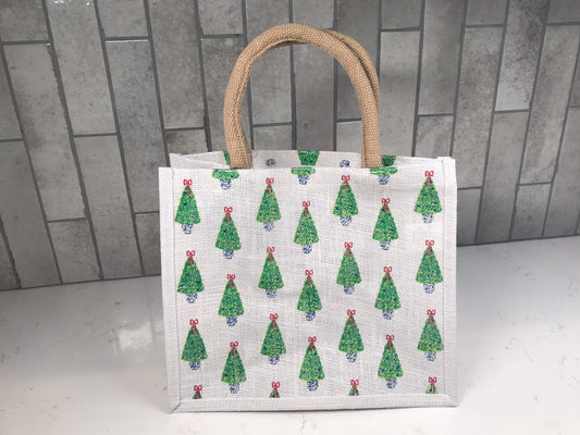 Medium holiday tote bag featuring allover Christmas tree pattern, neutral background and beige rope handles, shown standing on countertop.