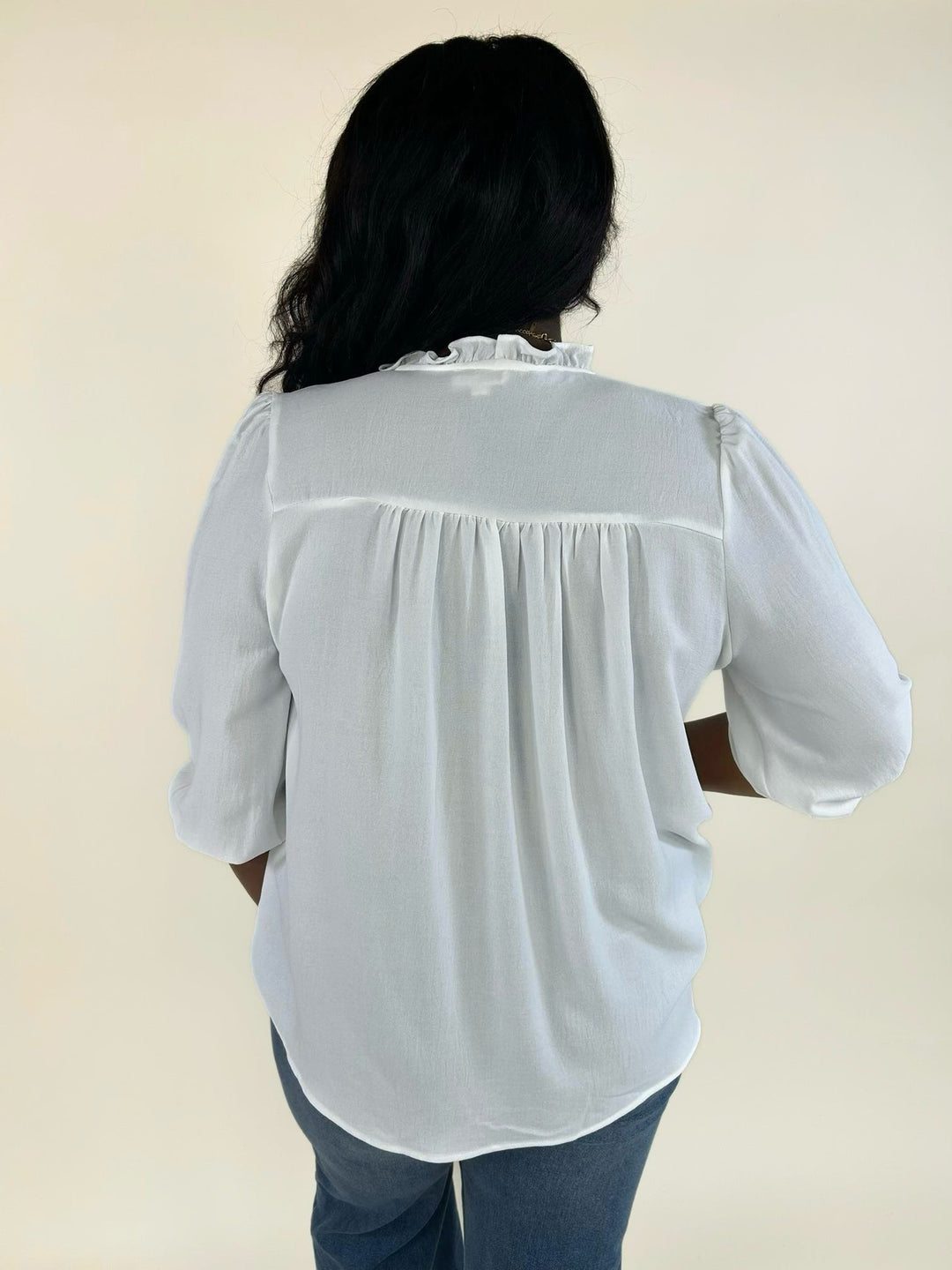 Back view of a white relaxed-fit ruffle trim blouse paired with wide-leg denim jeans.