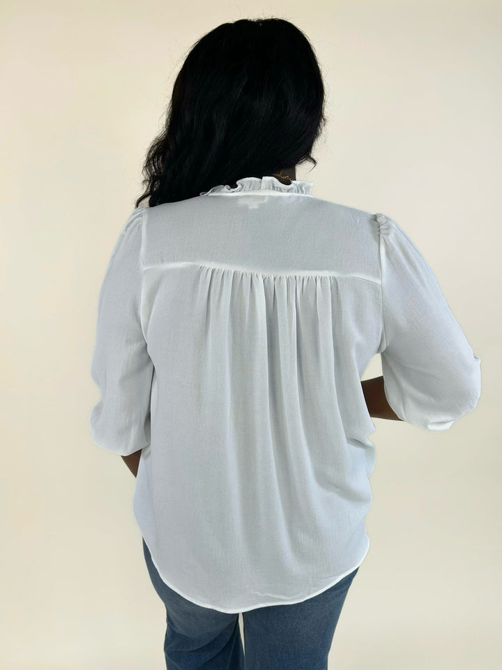 Back view of a white relaxed-fit ruffle trim blouse paired with wide-leg denim jeans.