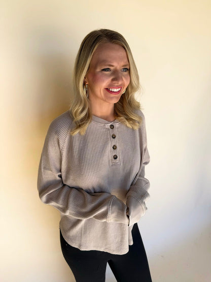 Woman wearing a dark taupe ribbed sweater against a plain background